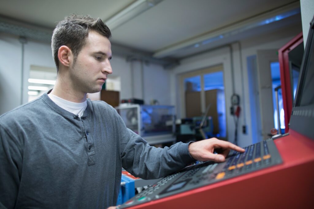 Young male technician using control panel for machine in workshop